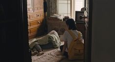 two people sitting on the floor in a room with wooden cabinets and drawers, one person is laying down