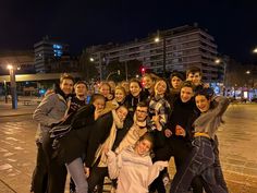 a group of people posing for a photo on the street at night time with buildings in the background