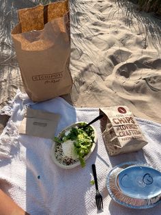 a table topped with a bowl of salad next to a bag of chips and a fork