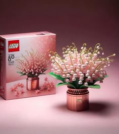 a pink vase with flowers in it next to a box that says lego 75 years