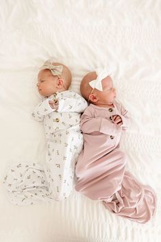 two babies laying next to each other on top of a white sheet covered bed together