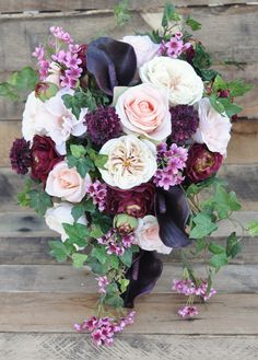 a bridal bouquet with purple and white flowers on a wooden bench in front of wood planks