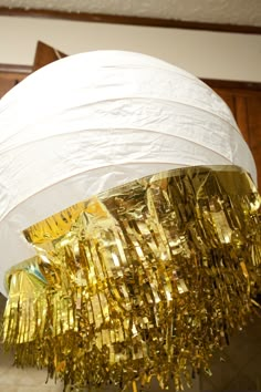 a white paper lantern with gold foil fringes hanging from it's sides and on the ceiling