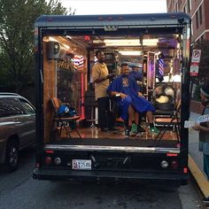 a man getting his hair cut in the back of a moving truck at an intersection