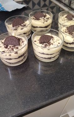 four desserts with oreo cookies and cream in small glass dishes on a counter