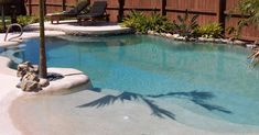 a pool with a palm tree in the middle and some chairs around it, next to a wooden fence