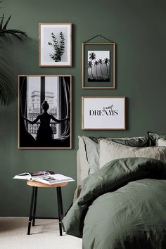 a bedroom with green walls and pictures on the wall above the bed, along with a small side table