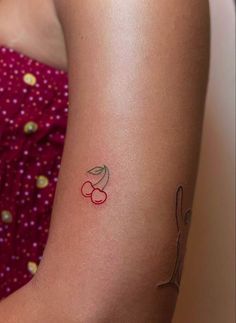 a woman's arm with a small cherry tattoo on the left side of her arm