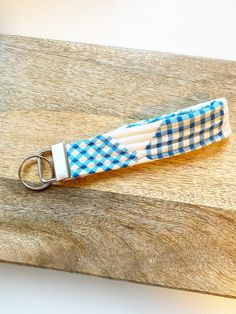 a blue and white checkered fabric keychain on a wooden board with a metal hook