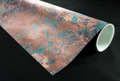 a roll of metallic foil with blue and pink paint on it's side, sitting on a black surface