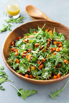 a wooden bowl filled with greens and carrots on top of a gray countertop