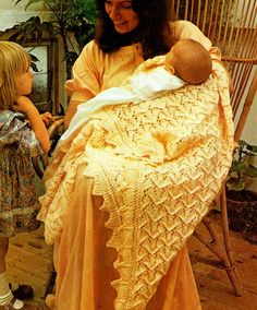 a woman holding a baby wrapped in a crochet blanket while sitting on a chair