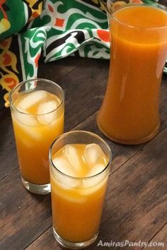 two glasses filled with orange juice sitting on top of a wooden table next to a pitcher