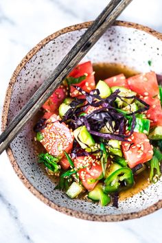 a close up of a bowl of food with chopsticks on the side and watermelon