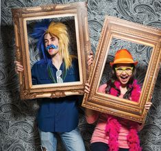 two people holding up framed pictures with their faces painted like wigs and moustaches