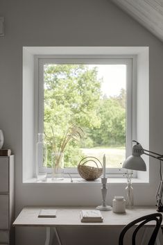 a desk with a lamp, vases and other items on it in front of a window