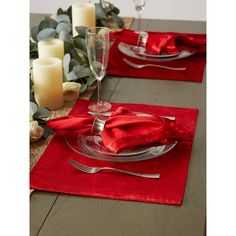 a place setting with red napkins, silverware and candles on a table cloth