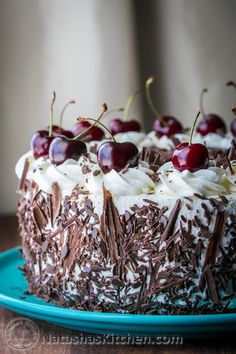 a cake with chocolate frosting and cherries on top is sitting on a blue plate