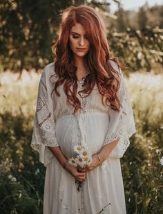 a woman with long red hair wearing a white dress and holding a flower in her hand