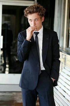 a young man in a suit and tie is posing for the camera with his hand to his mouth