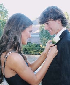 a young man and woman standing next to each other in front of a house with trees