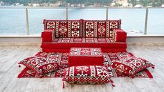 a red couch sitting on top of a wooden floor next to a body of water