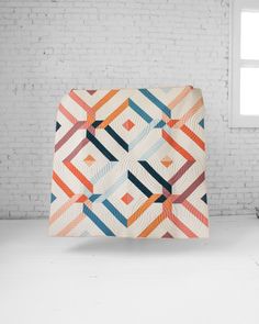 a white brick wall with an orange, blue and red quilt on it's side