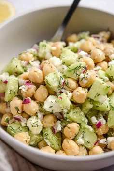 a white bowl filled with chickpeas and cucumber salad next to a lemon wedge