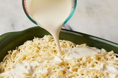 a green bowl filled with noodles and cream being poured into the mixture to make it