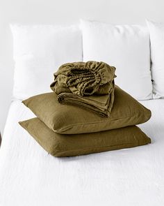 three pillows stacked on top of each other in front of a bed with white sheets