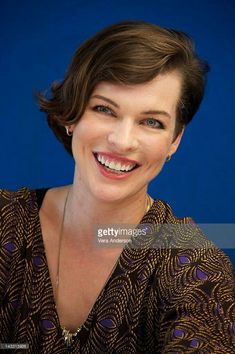 a smiling woman with dark hair and blue eyes, wearing a brown dress smiles at the camera