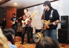 three young men are playing guitars in front of a group of people on the stage