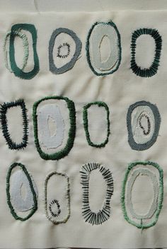 an embroidered piece of cloth with green and white designs on it, including oval shapes