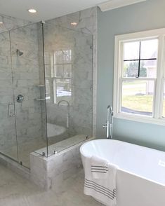 a white bath tub sitting next to a window in a bathroom with marble walls and floors