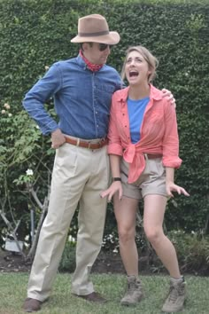 a man and woman standing next to each other in front of a hedge with their mouths open