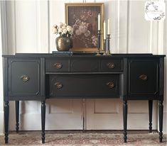 a black dresser with two drawers and candles on it in front of a white wall