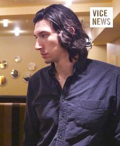 a man with long hair is standing in front of a wall full of glass balls