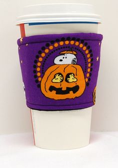 a purple cup sleeve with a pumpkin on it and a ghost in the middle, sitting next to a coffee cup