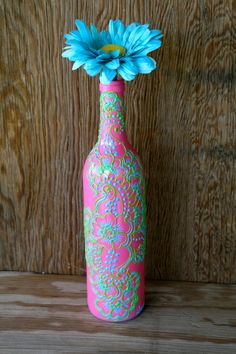 a pink vase with a blue flower in it sitting on a wooden table next to a wood paneled wall