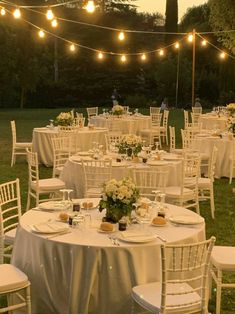 tables and chairs are set up for an outdoor dinner in the grass with lights strung above them