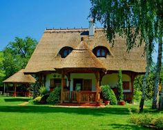 a small house with a thatched roof in the middle of a green lawn area