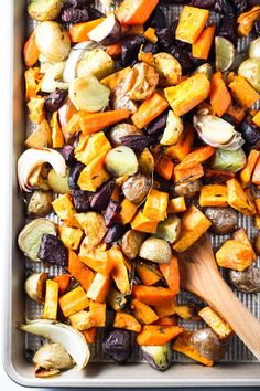 roasted vegetables in a baking pan with a wooden spoon