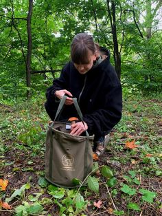 a woman in the woods looking at her cell phone while holding a tote bag