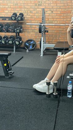 a woman is sitting on the ground in front of a gym machine and taking a selfie with her cell phone