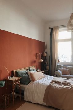 a bedroom with an orange accent wall and white bed in the corner, next to a window