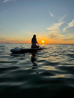 a person on a surfboard in the water at sunset or dawn, with the sun setting behind them