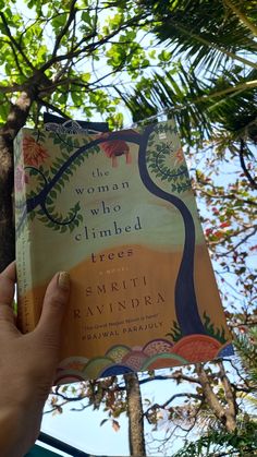 the woman who climbed tree by smriti ravidra is holding up a book