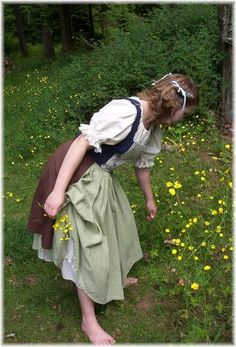 a woman bending over in the grass with yellow flowers around her and looking at something