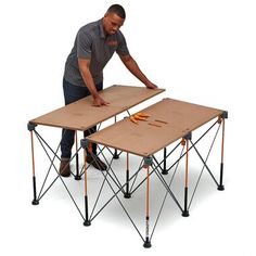 a man standing over two folding tables on top of eachother with tools in it