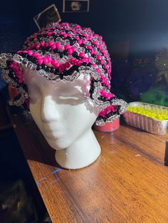 a white mannequin head wearing a pink and black hat on top of a wooden table